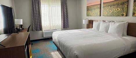 A hotel room with a large bed, a desk with a telephone, a chair, a window with curtains, and two wall-mounted lamps.
