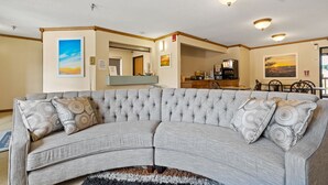 A living room with a grey sectional sofa, two patterned throw pillows, a coffee table, and a rug. There are ceiling lights, a painting on the wall, and a kitchen area in the background. - Days Inn by Wyndham Wall (Wall)