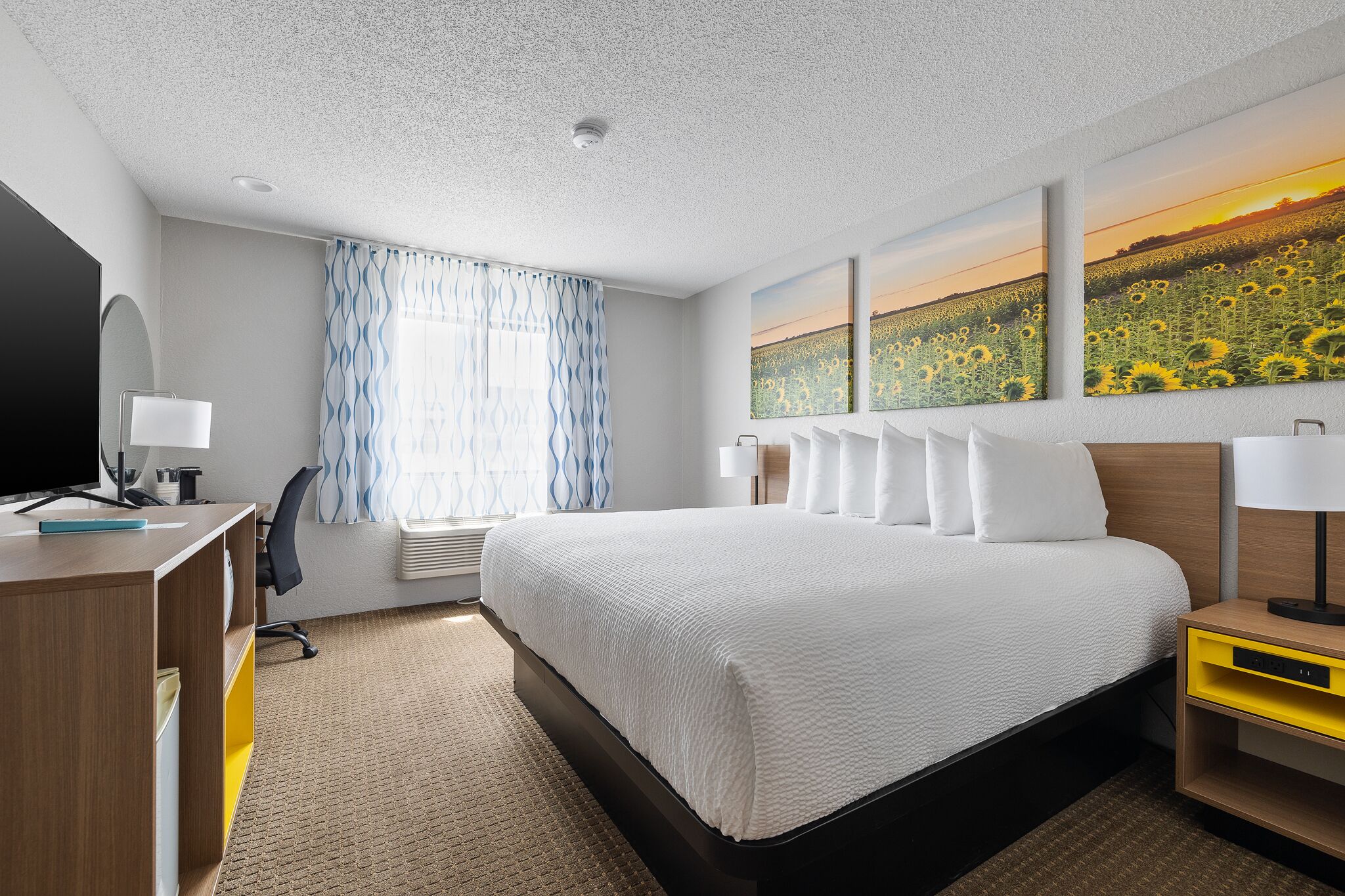 A hotel room with a large bed, a desk with a computer, a chair, a TV, and a window with curtains.