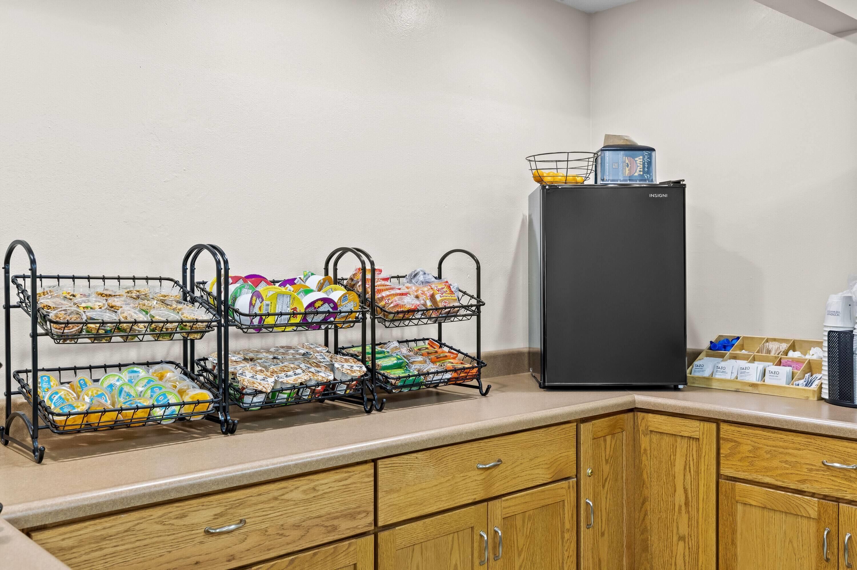 Una kitchenette con un refrigerador, un escurridor de alambre de tres niveles con alimentos y armarios de madera.