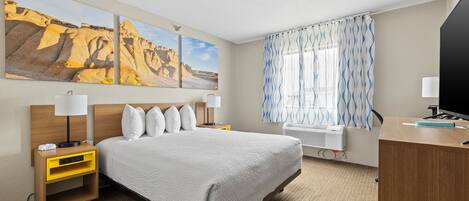Habitación de hotel con cama, mesitas de noche, escritorio, televisor y grandes pinturas de paisajes desérticos en la pared.