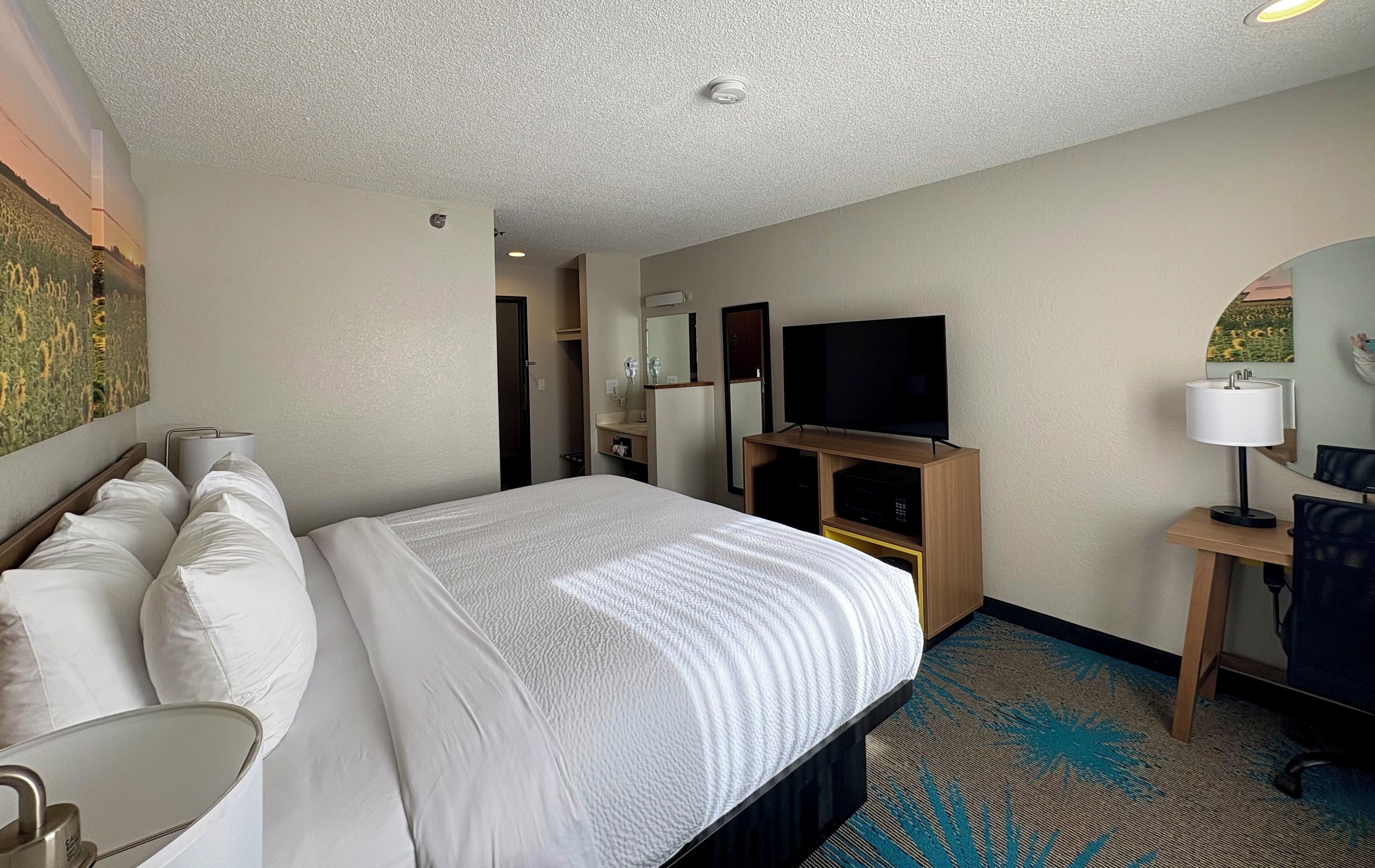 Habitación de hotel con una cama grande, televisor, escritorio con lámpara y espejo.