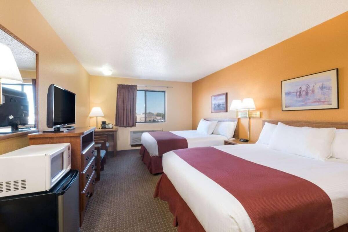 A hotel room with two beds, a television, a microwave, and a window with curtains.