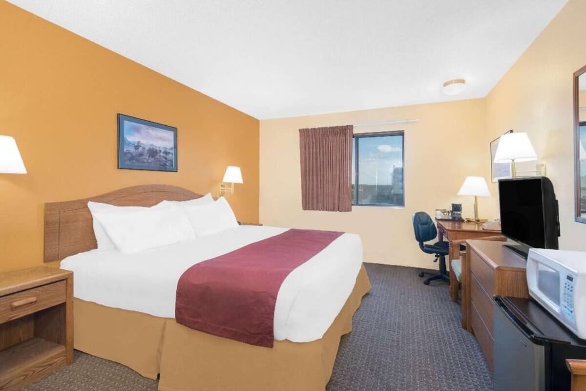 A hotel room with a bed, desk, TV, and a window with curtains.