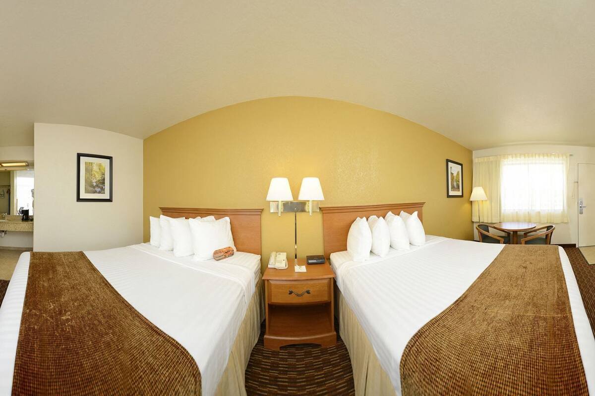 A hotel room with two beds, a desk, a chair, a TV, a mini-fridge, and a bathroom.