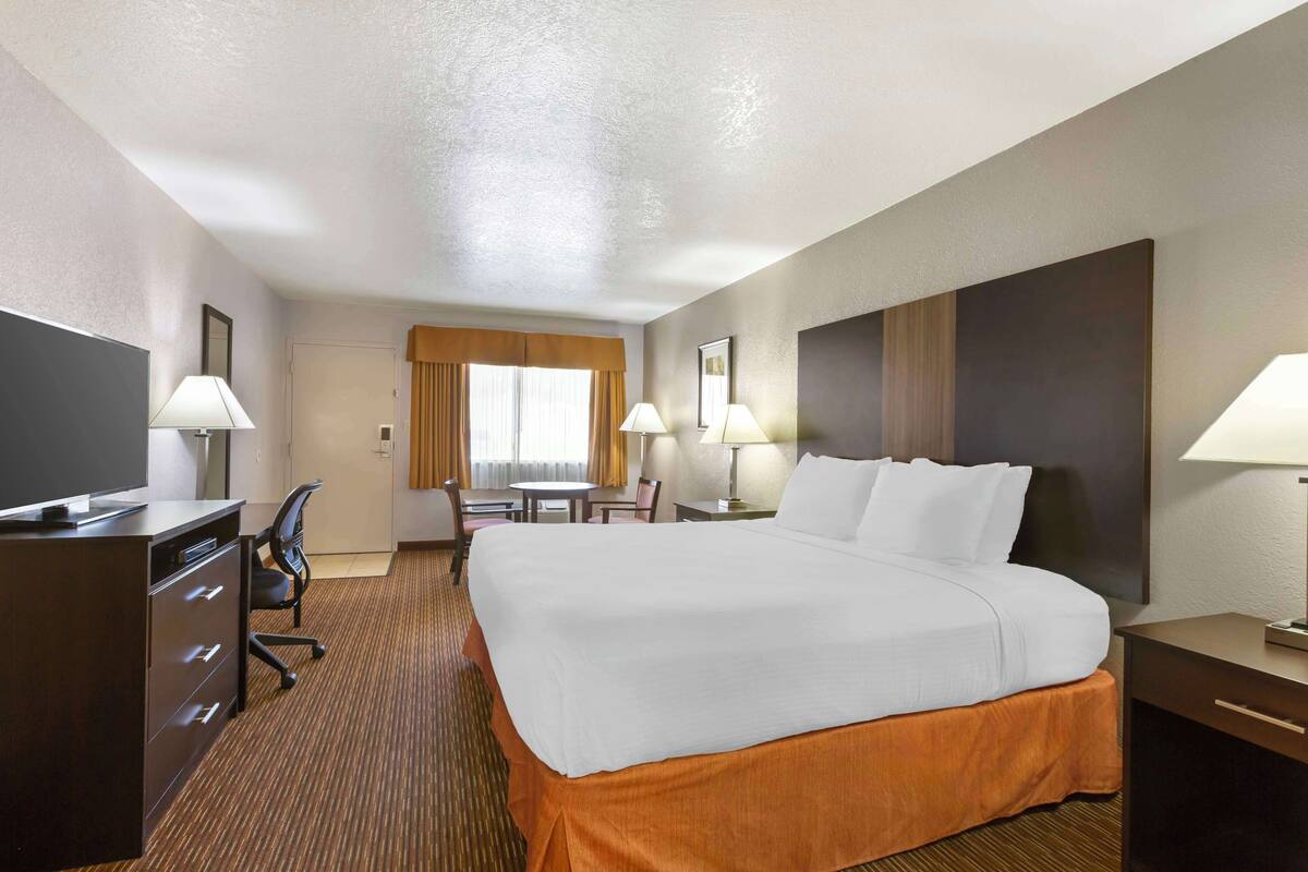 A hotel room with a large bed, a desk with a chair, a television, and two lamps.