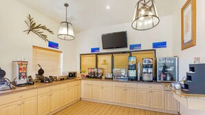 Un'area della reception di un hotel con un bancone, una TV a schermo piatto e diversi servizi, come una macchina del caffè e un espositore di frutta.