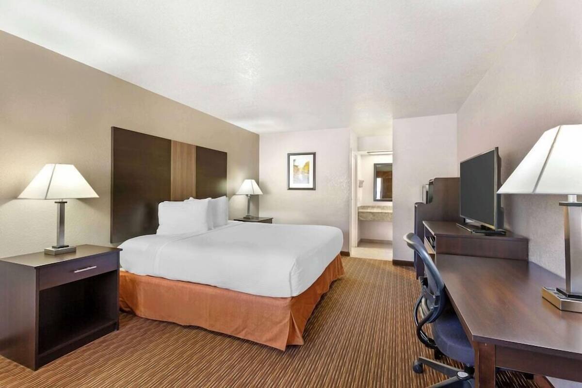 A hotel room with a large bed, two bedside tables with lamps, a desk with a chair, and a television.