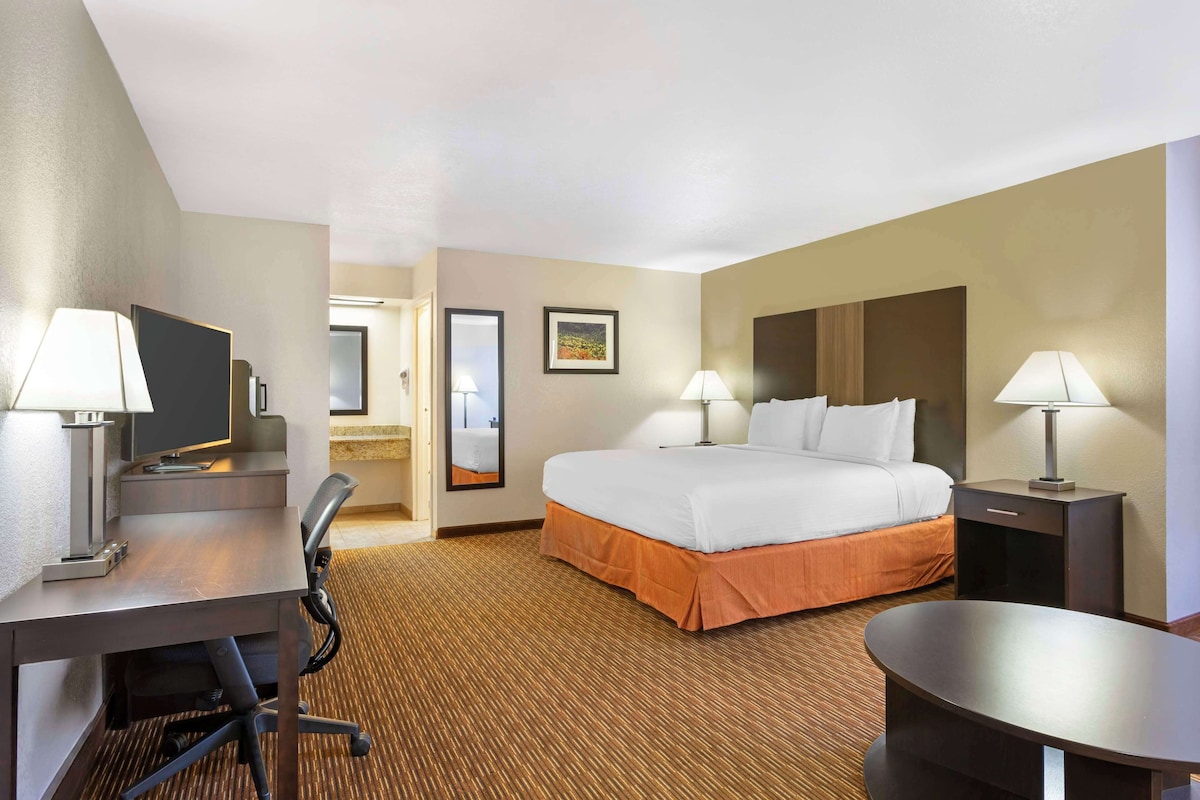 A hotel room with a bed, desk, chair, lamps, and a small table.