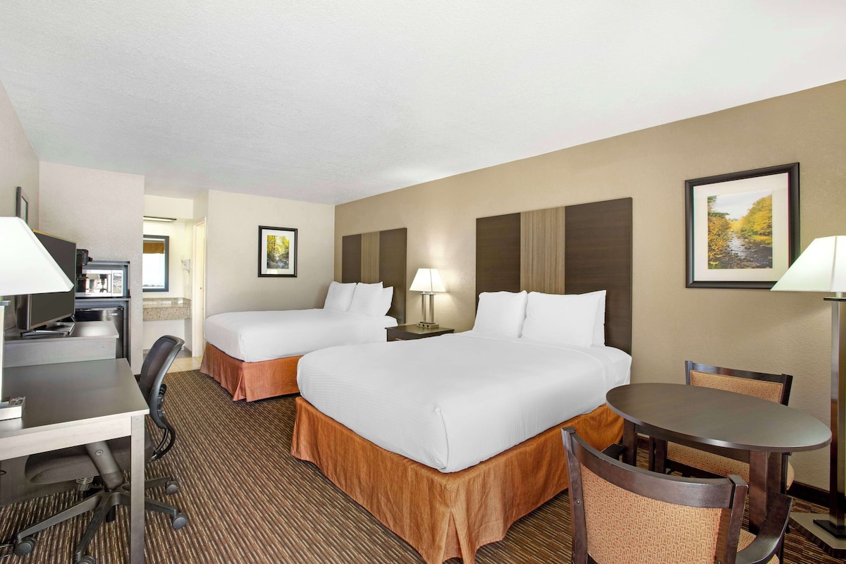 A hotel room with two beds, a desk, a chair, a table, and a lamp.