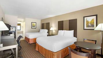 A hotel room with two beds, a desk, a chair, a table, and a lamp.