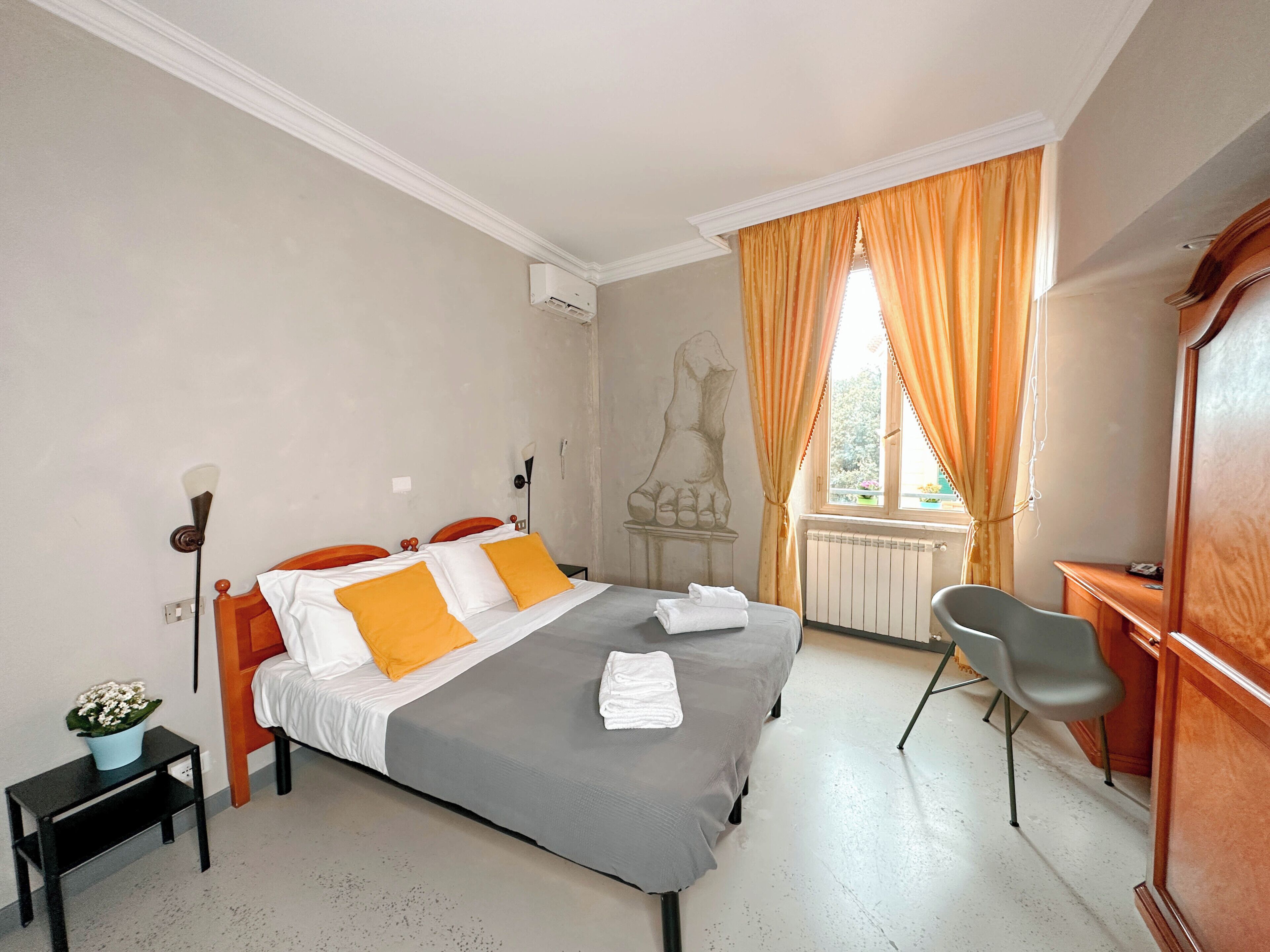 A bedroom with a bed, a desk, a chair, a radiator, and a window with curtains.