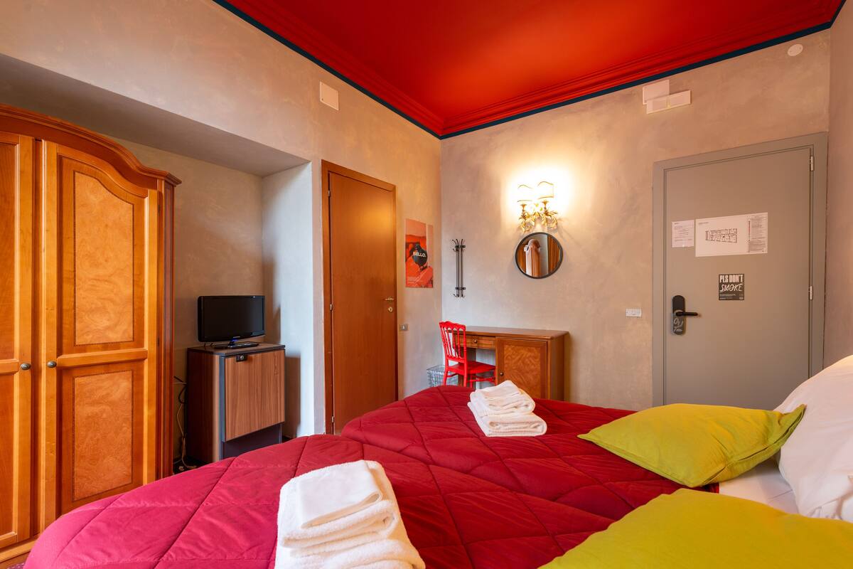 Une chambre d’hôtel avec une couvre-lit rouge, une armoire en bois, une télévision et un bureau avec une chaise.