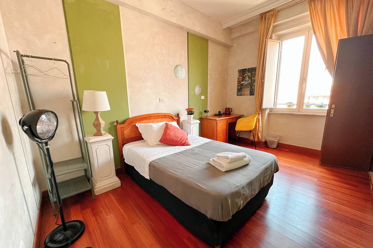 Une chambre à coucher avec un lit, un bureau, une chaise, un radiateur et une fenêtre avec des rideaux.
