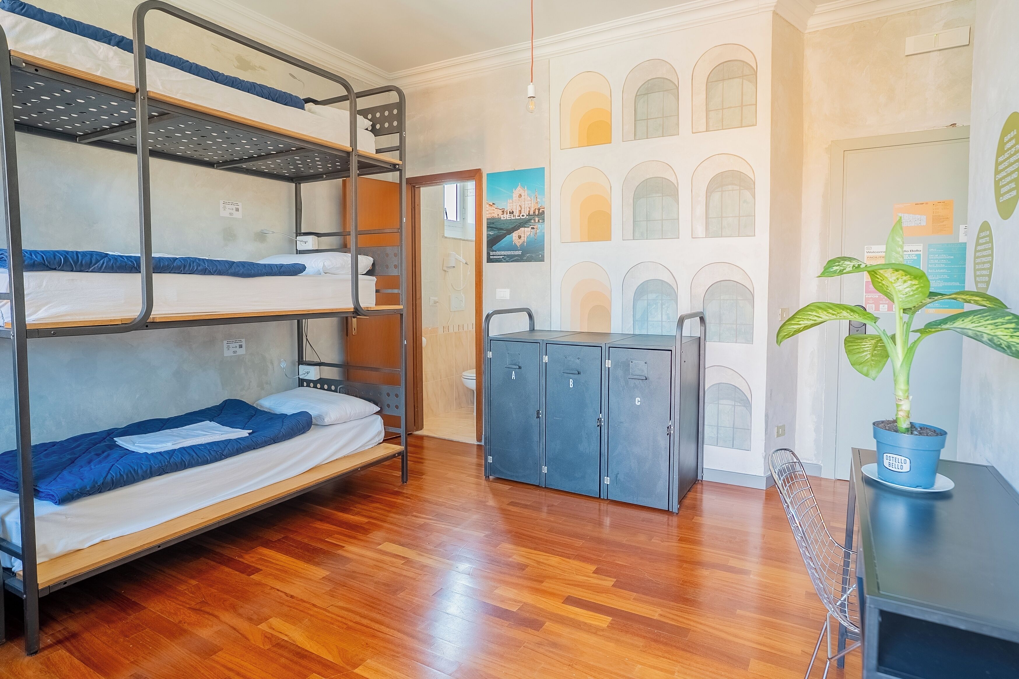 A bunk bed room with a wooden floor, a desk with a potted plant, and a door with a poster.