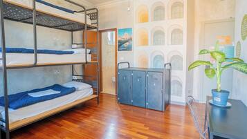 A bunk bed room with a wooden floor, a desk with a potted plant, and a door with a poster.
