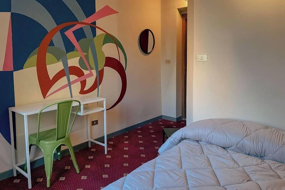 Une chambre d’hôtel avec un lit, un bureau et une œuvre d’art abstraite et colorée accrochée au mur.