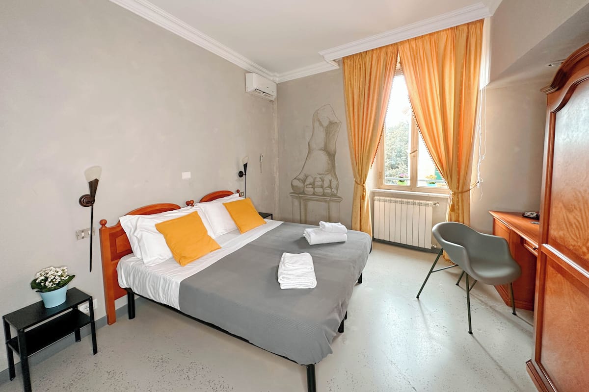 A bedroom with a bed, a desk, a chair, a radiator, and a window with curtains.