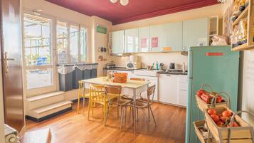 Una cocina con mesa, sillas, refrigerador y ventana con vista al exterior.