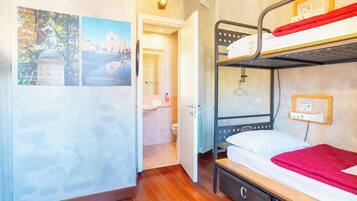 A bunk bed room with a wooden floor, a radiator, a hanging light fixture, and a framed picture on the wall.