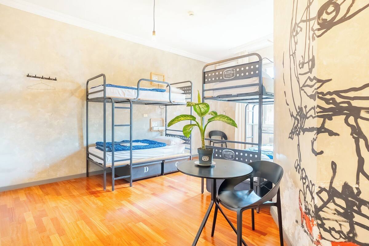 Une chambre de dortoir avec des lits superposés, une table ronde, une chaise et une plante en pot.