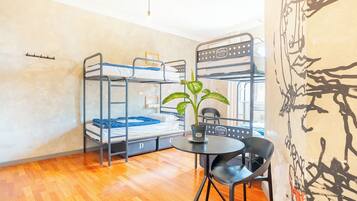 Un dormitorio con literas, una mesa redonda, una silla y una planta en maceta.