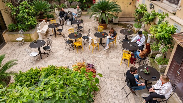 Un patio al aire libre con varias mesas y sillas, rodeado de plantas en macetas y follaje.