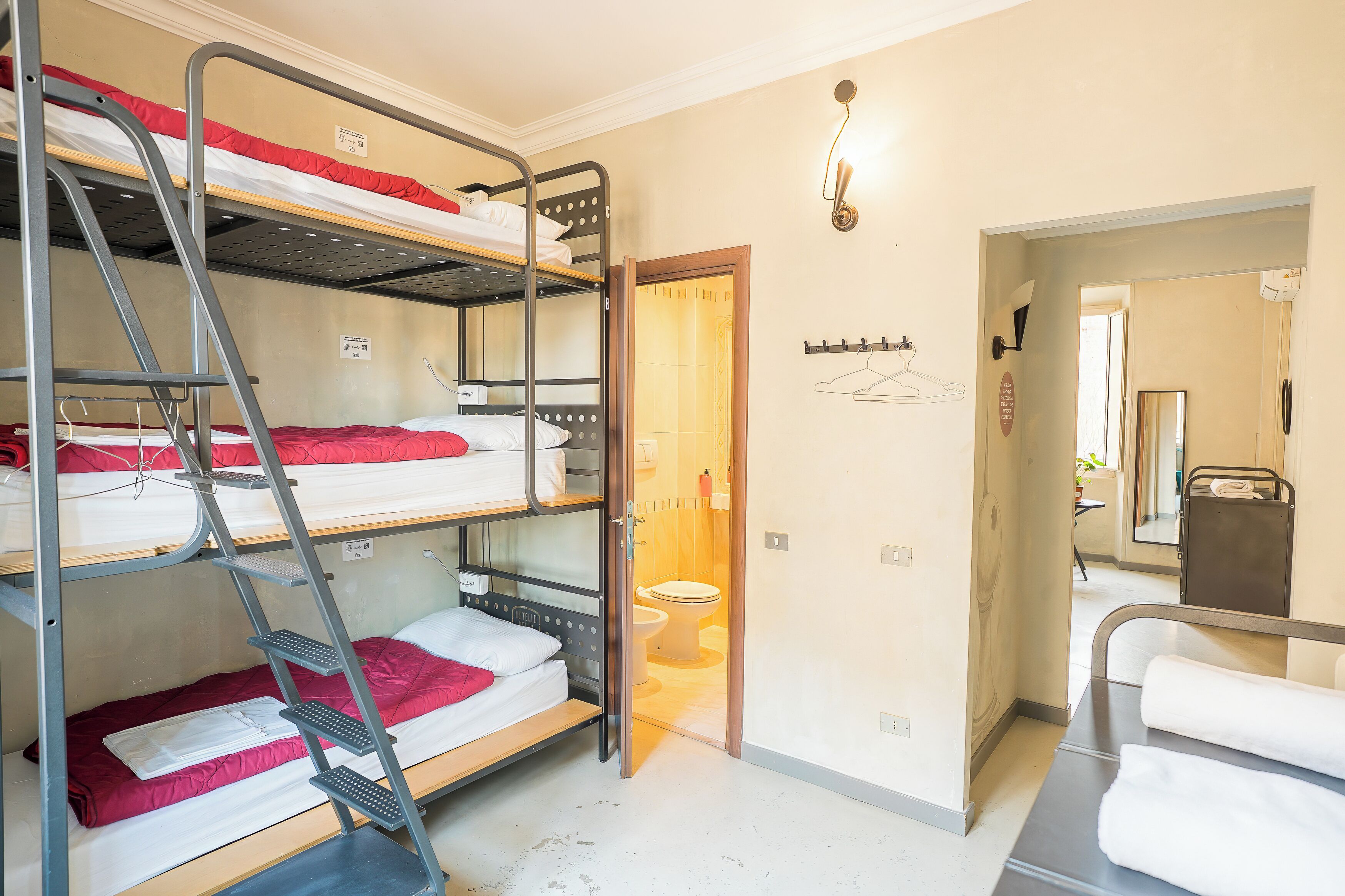 Een slaapkamer met een stapelbed, een houten deur naar een badkamer en een kapstok met hangers.