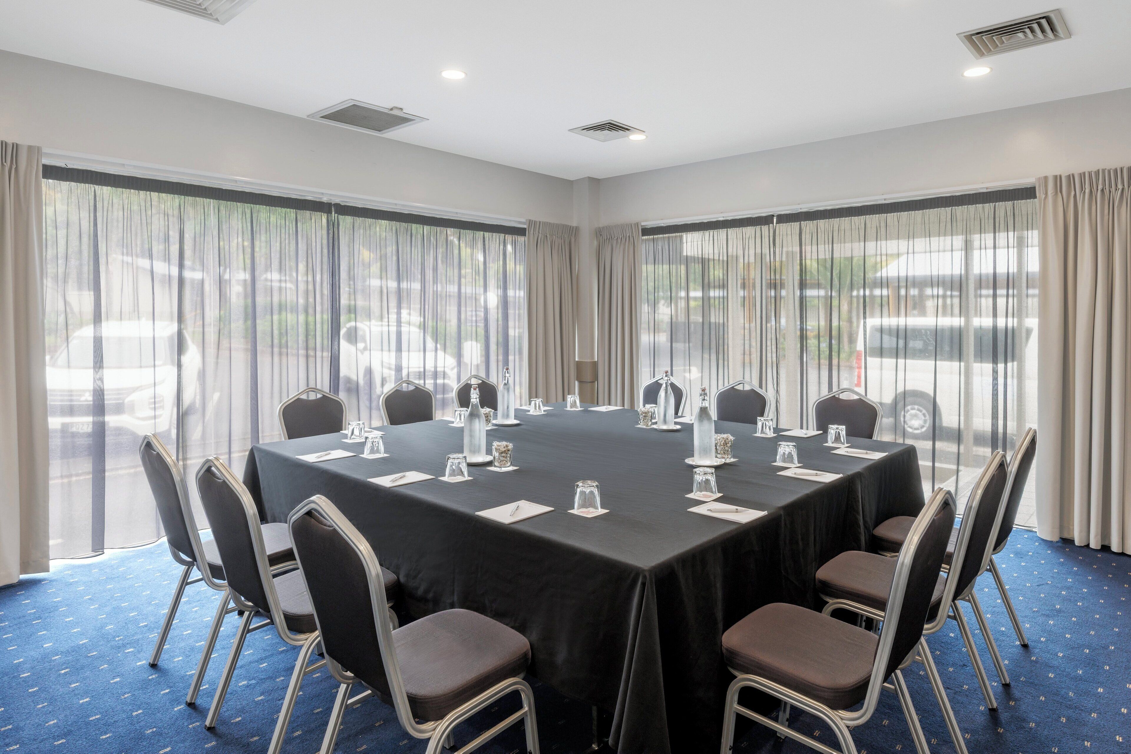 Une salle de conférence avec une table noire, des chaises blanches et un tapis bleu.