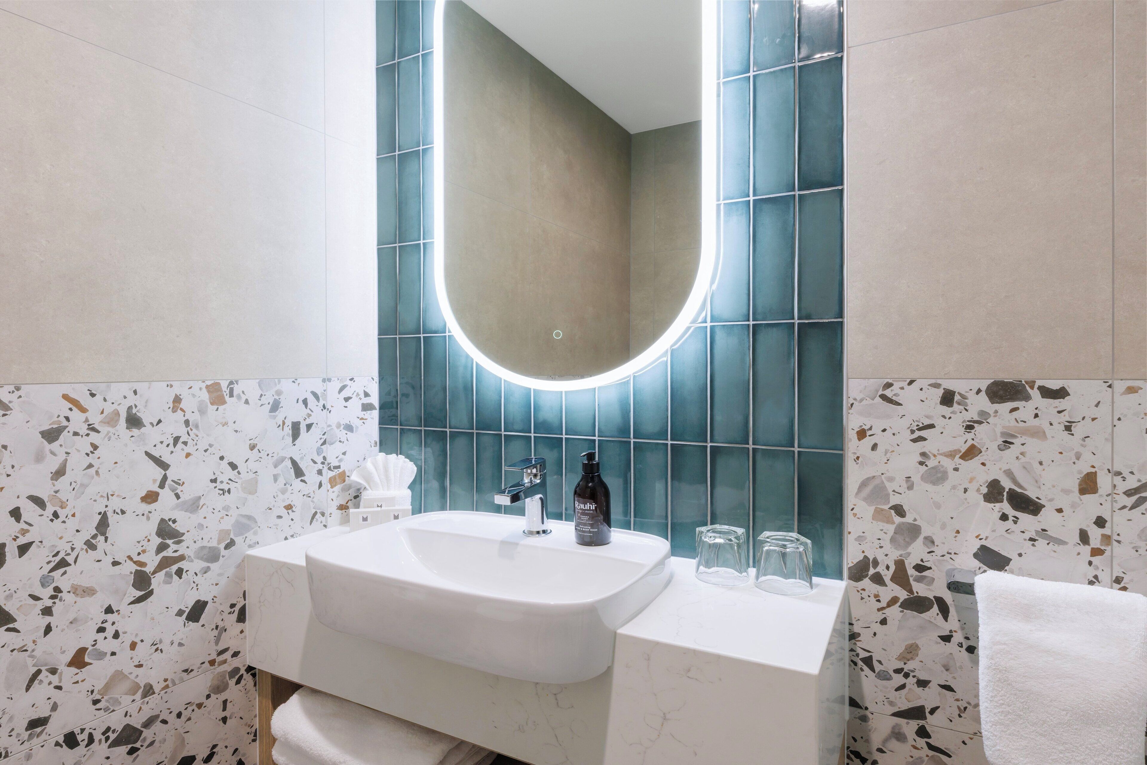 Un baño con lavamanos blanco, espejo y toallero.