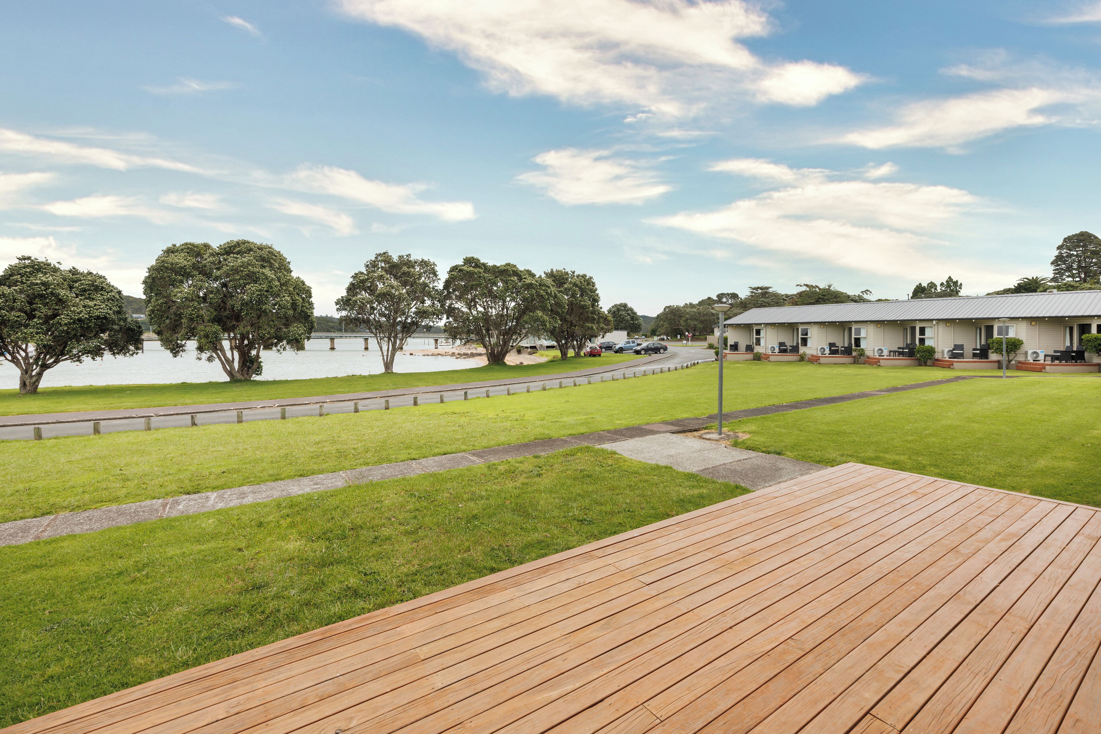 A wooden deck overlooking a grassy area with a lake and a row of buildings in the background.