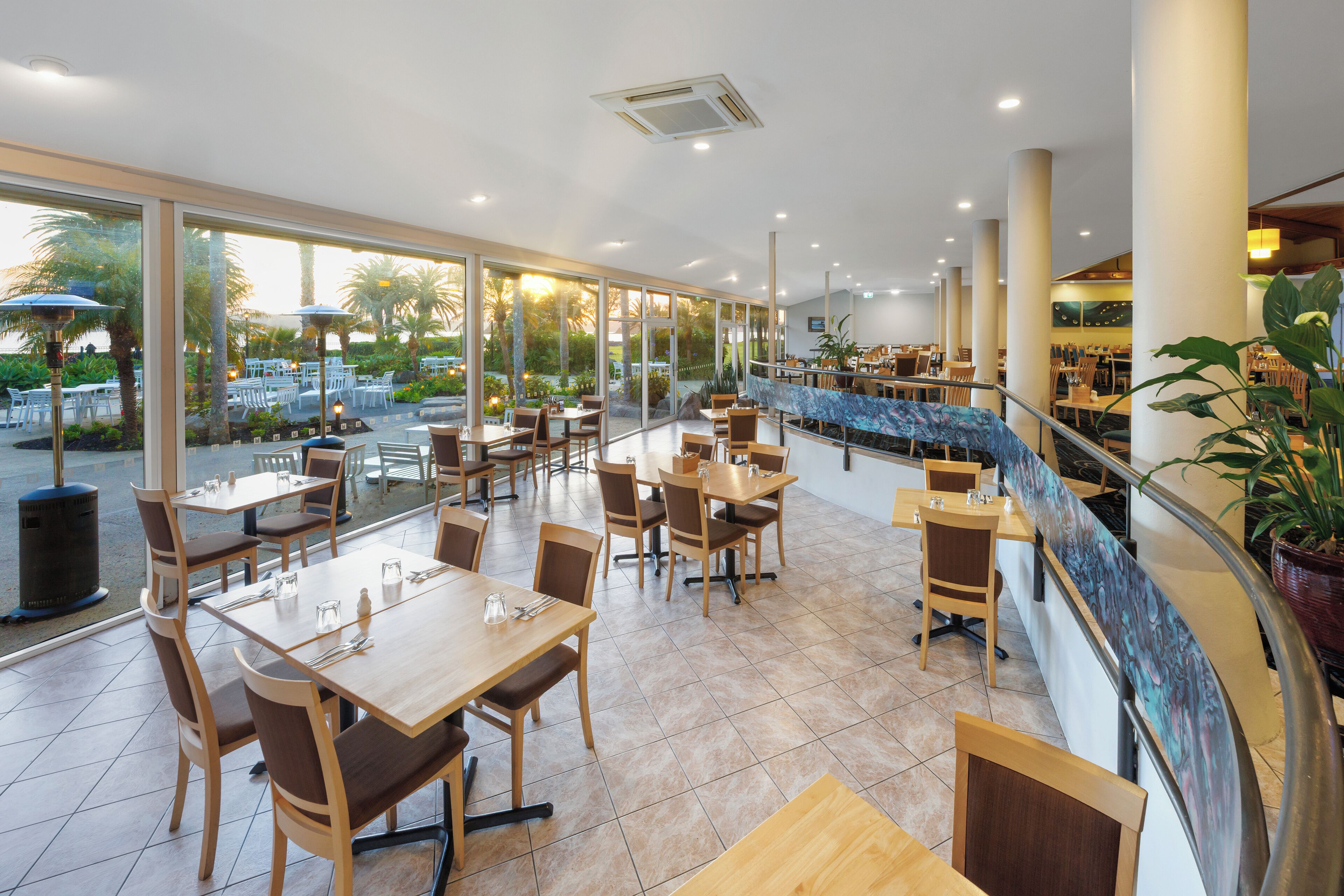 A spacious restaurant with large windows, wooden tables, and chairs.
