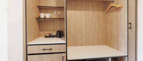 A wooden wardrobe with a shelf holding cups and glasses, a hanging rack, and a flat surface with a coffee maker.