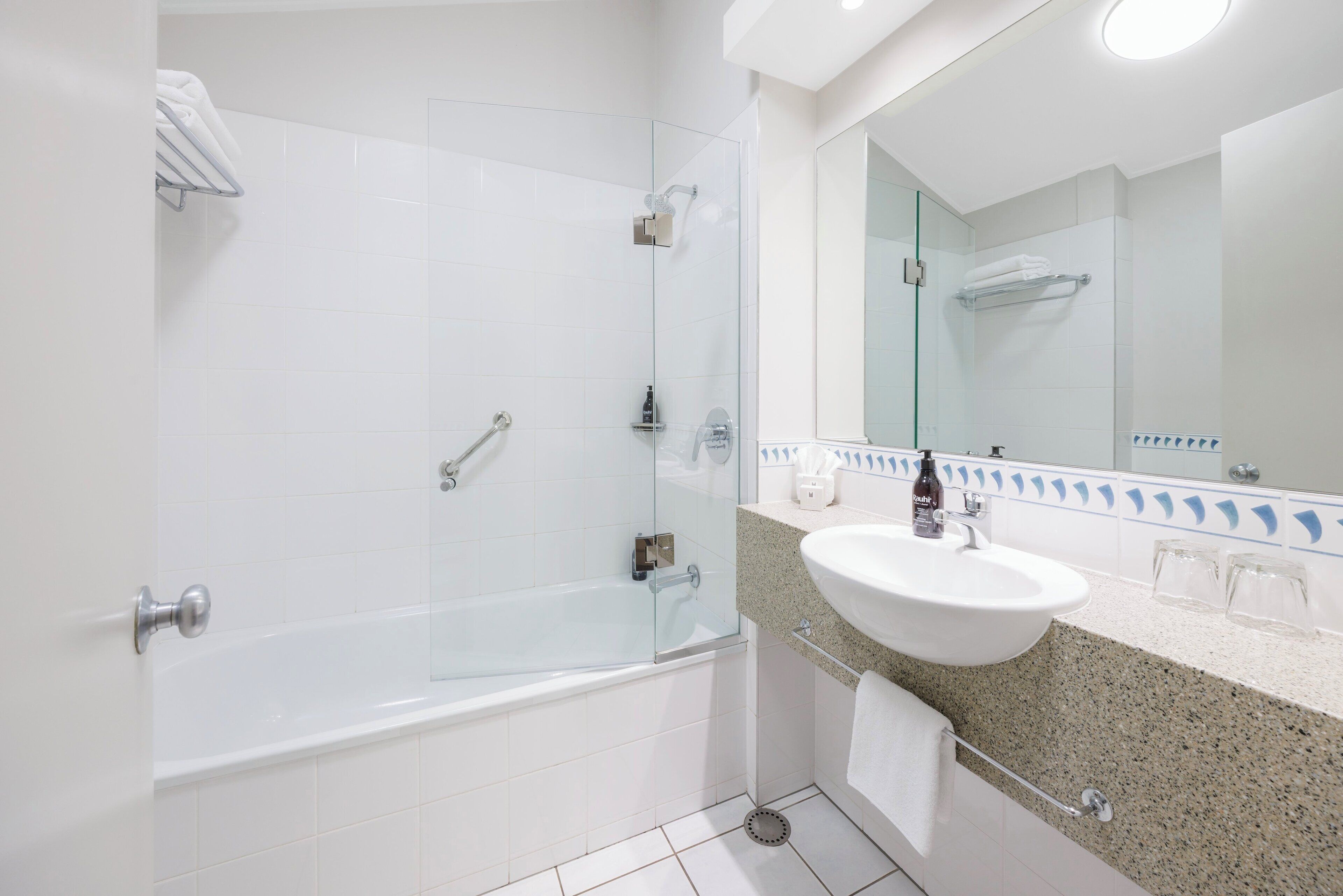Un baño moderno con ducha envuelta en vidrio, una bañera blanca, lavamanos con encimera de granito y un espejo grande.