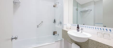 Un baño moderno con ducha envuelta en vidrio, una bañera blanca, lavamanos con encimera de granito y un espejo grande.