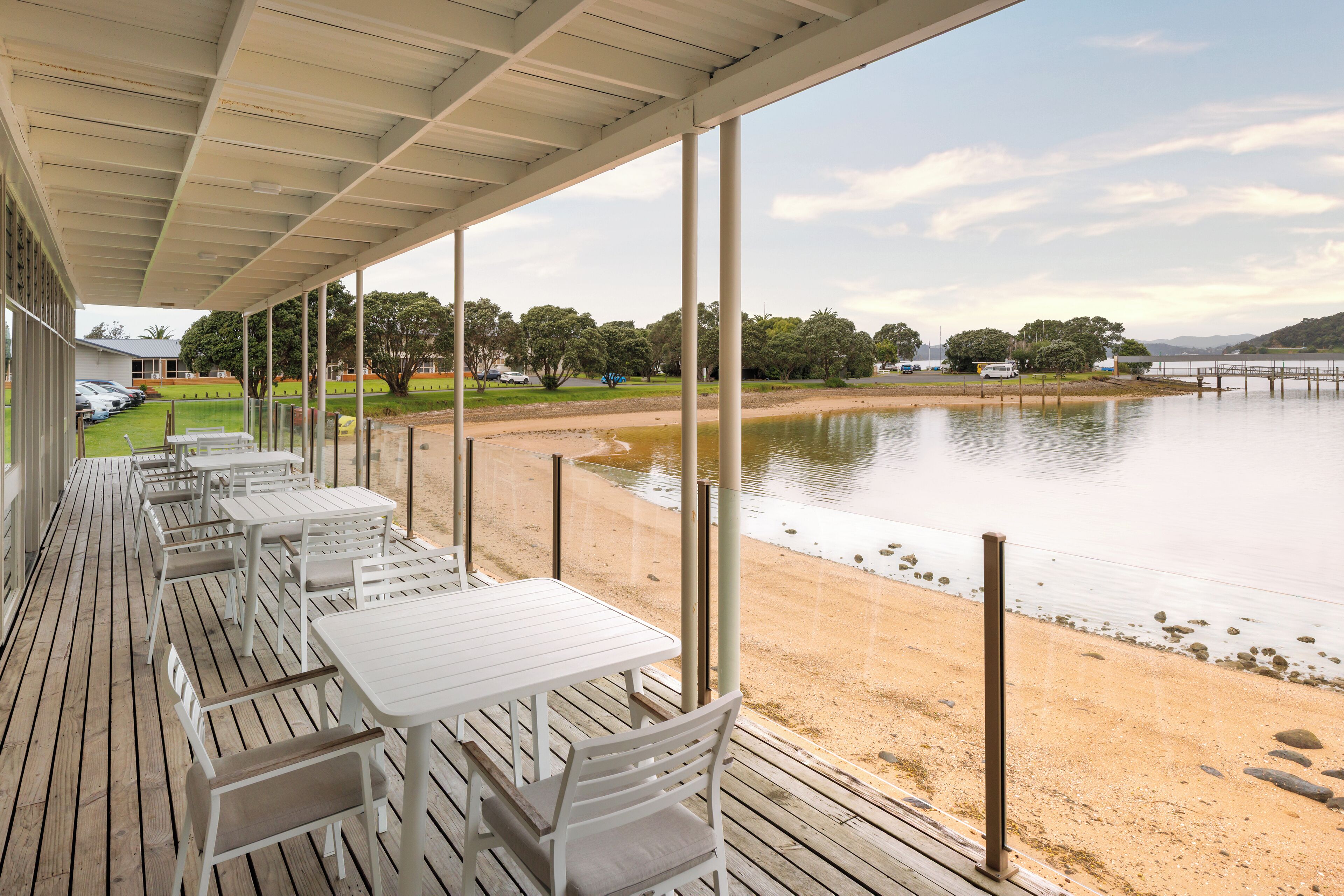 A covered outdoor seating area with tables and chairs overlooking a lake and beach.