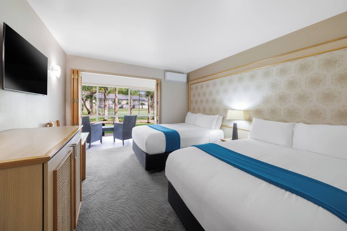 A hotel room with two beds, a desk, a TV, and a view of the outdoors.