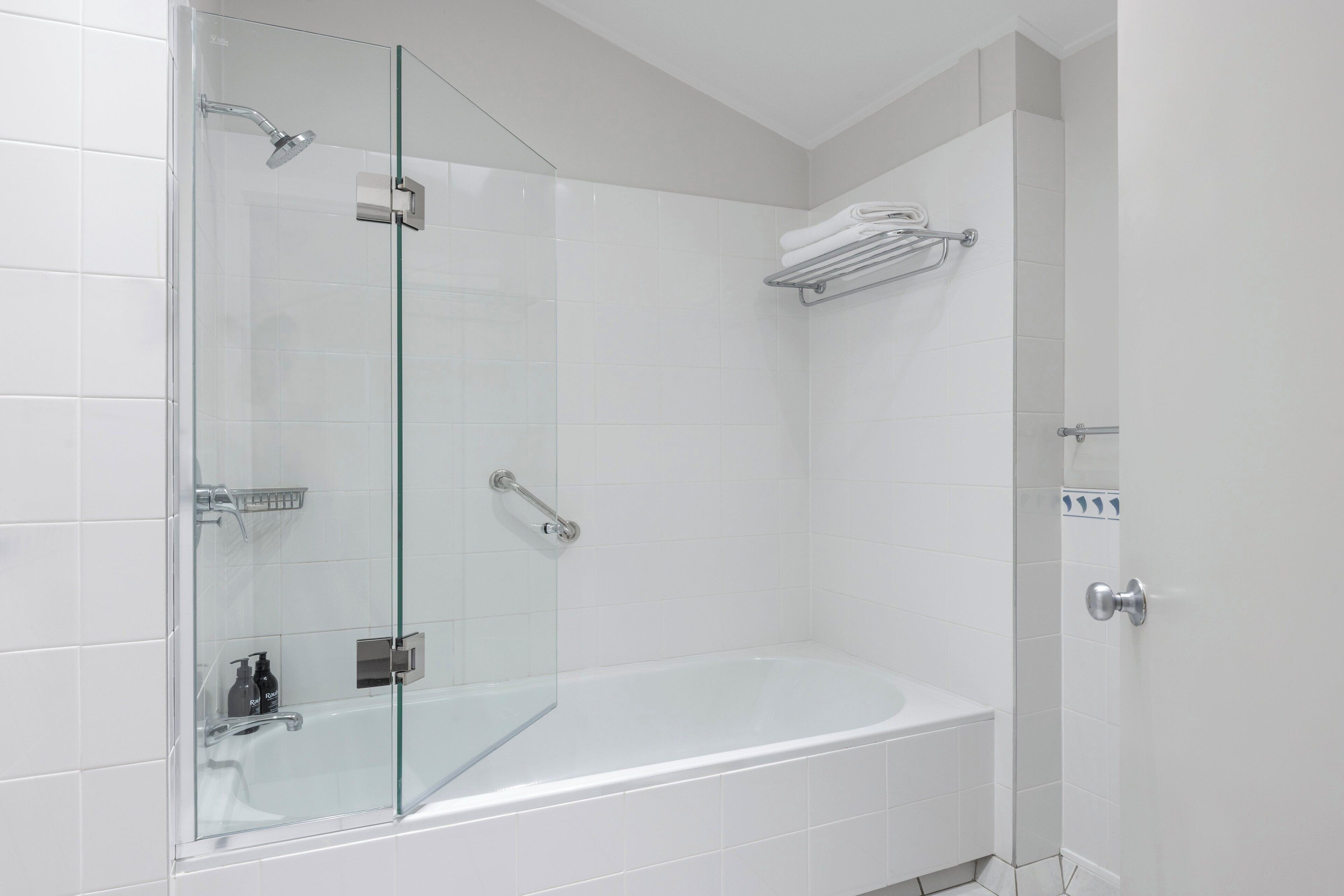 A modern bathroom with a glass-enclosed shower, a white bathtub, and a towel rack.