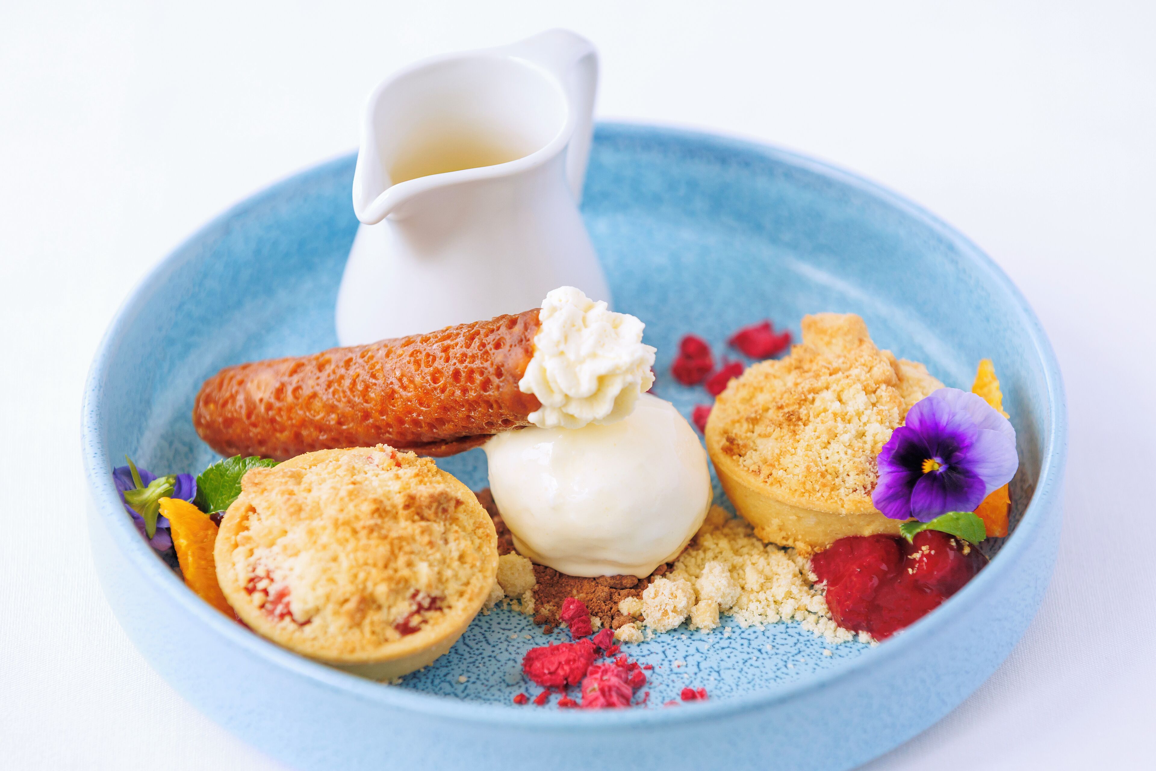 A dessert plate with various items including a pastry, a scoop of ice cream, and a small pitcher.
