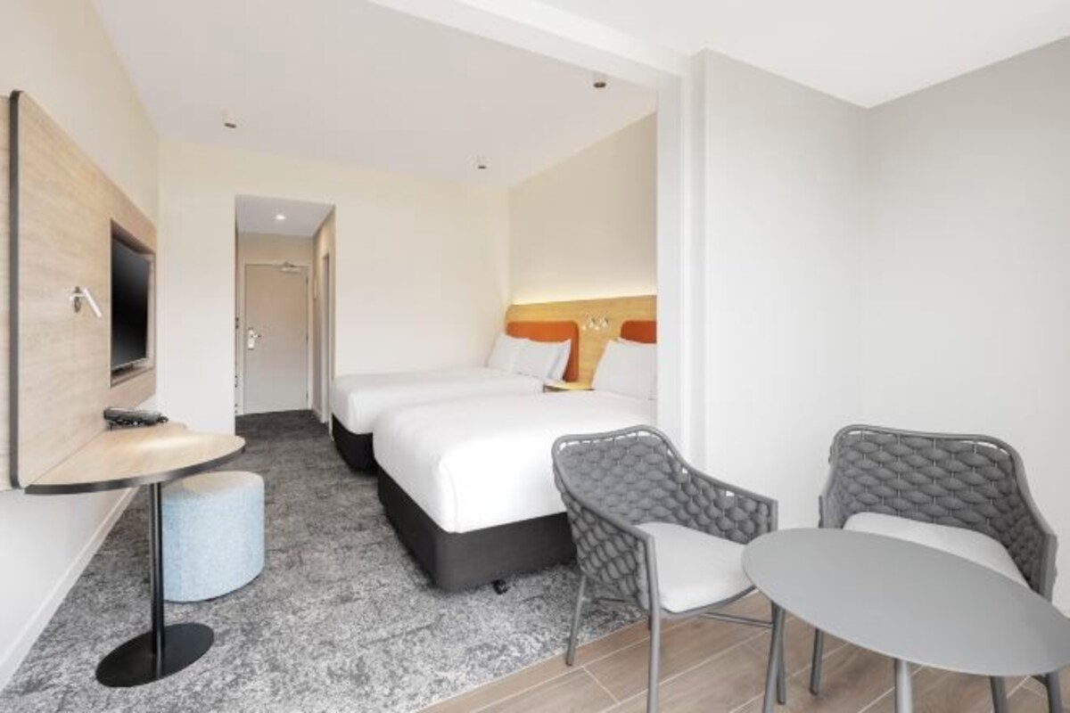 A hotel room with a bed, a small table, two chairs, a TV, and a bathroom door.