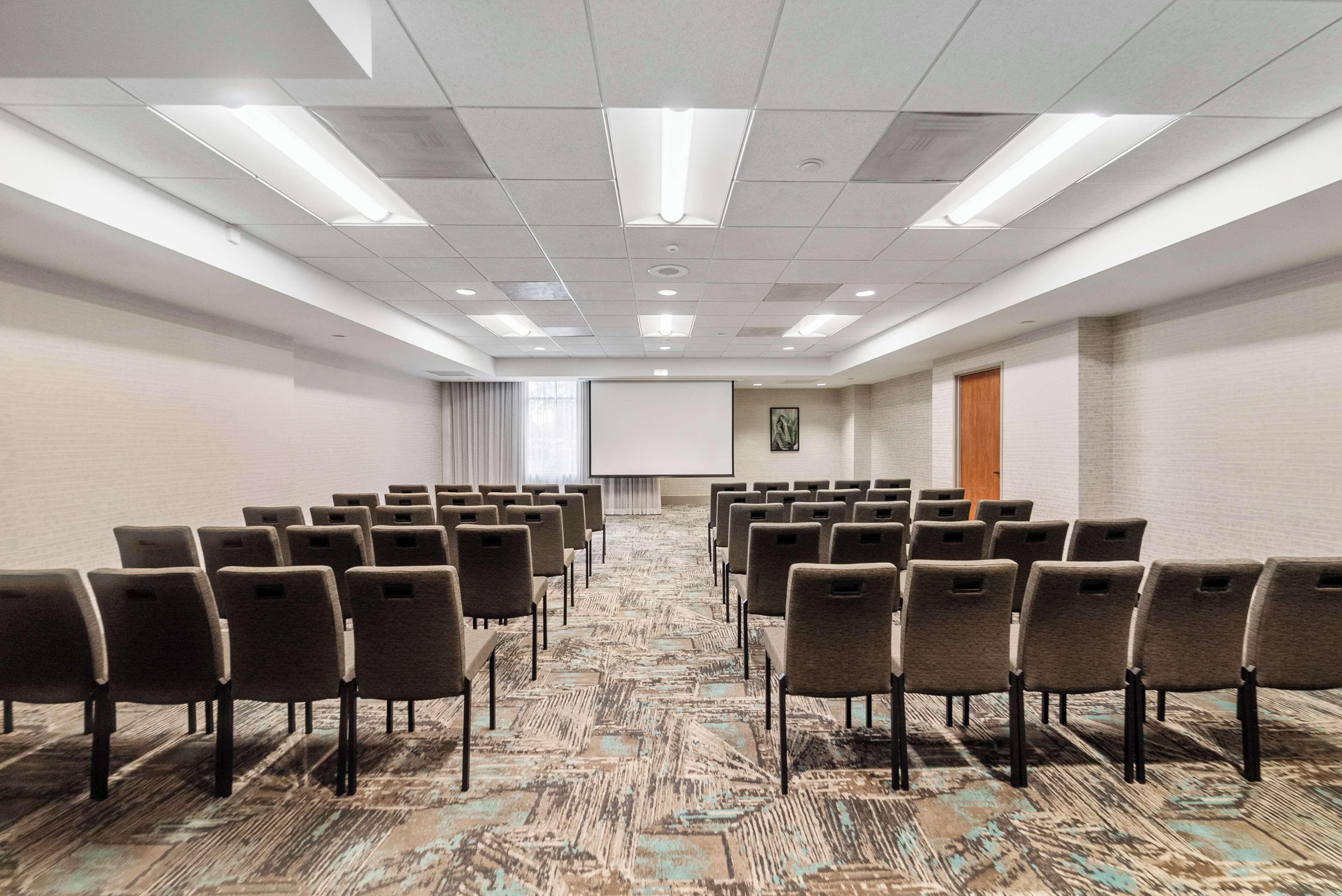 A conference room with rows of chairs, a projector screen, and a carpeted floor.