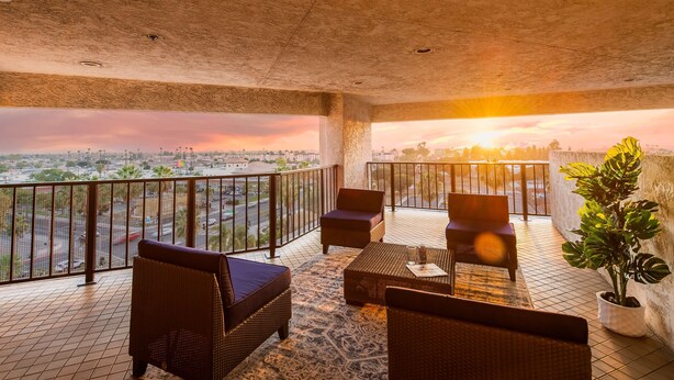 A balcony with wicker furniture, a potted plant, and a view of the cityscape at sunset. - DoubleTree by Hilton Carson (Carson)
