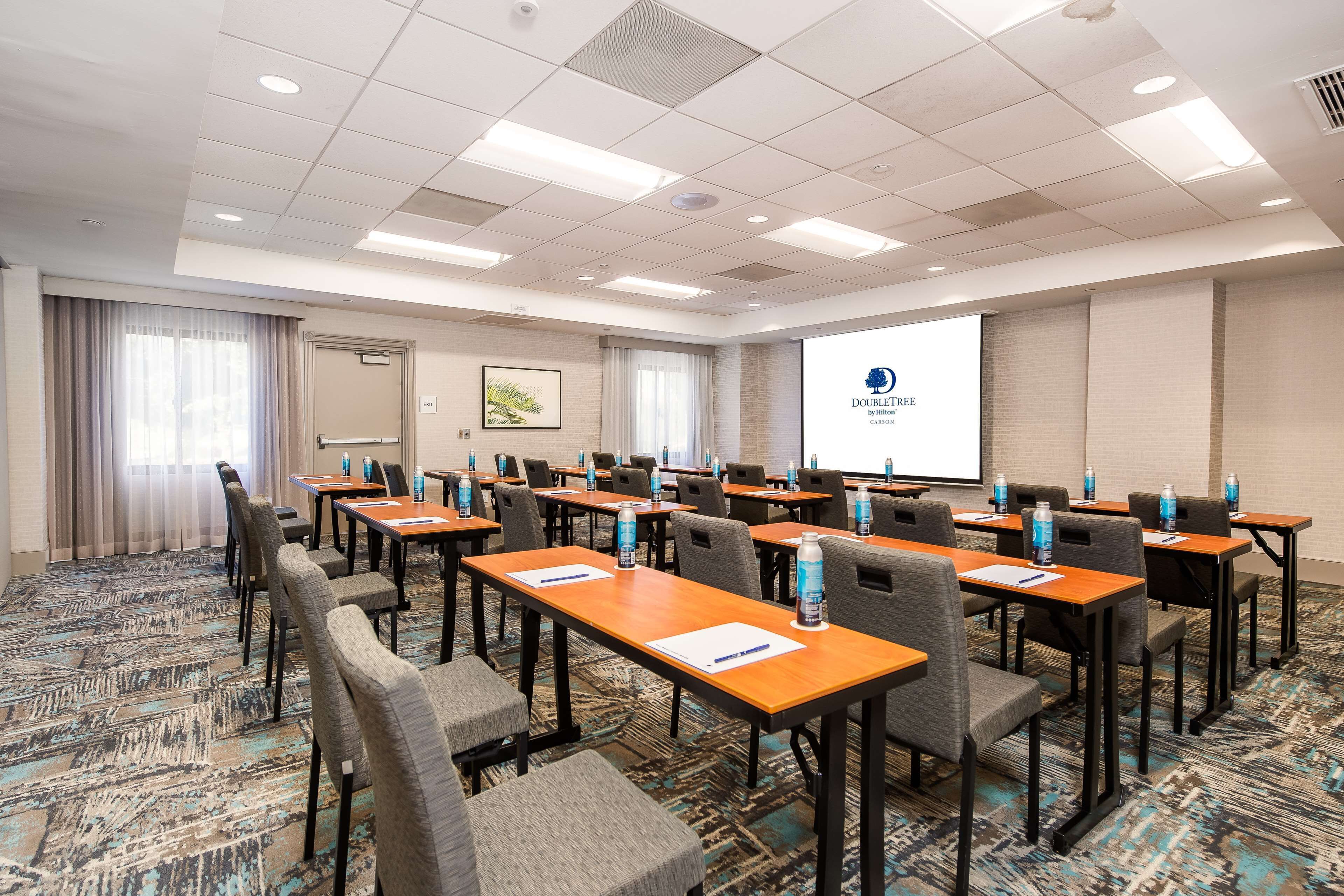 A conference room with multiple tables and chairs, a projector screen displaying a logo, and a carpeted floor.