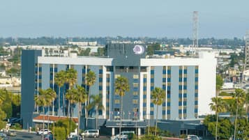 A large, multi-story hotel with a prominent logo on the roof, surrounded by a parking lot and palm trees.