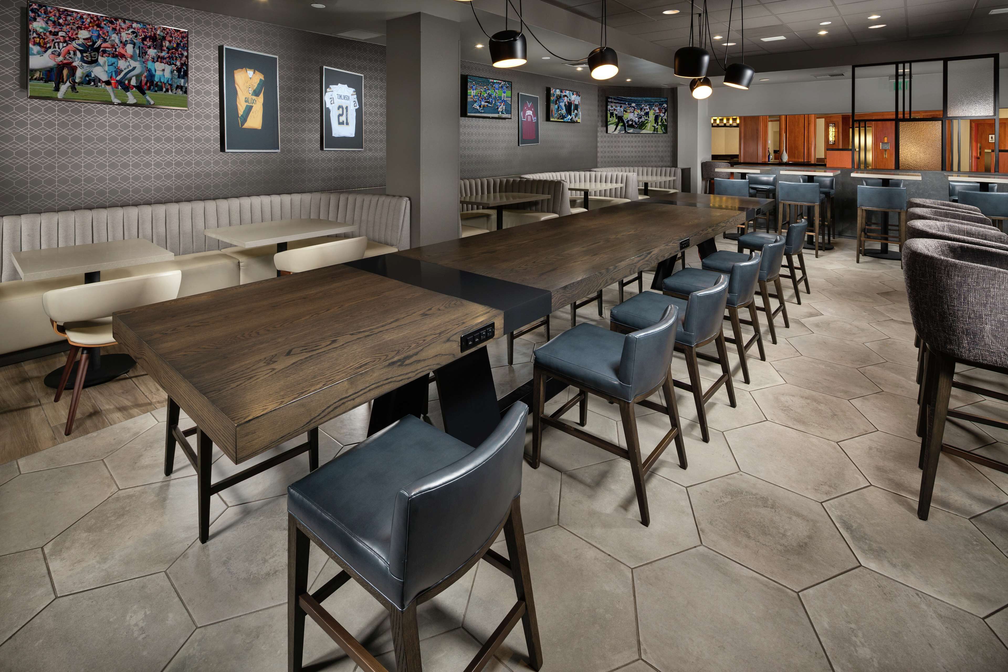 Ein Restaurant mit langen Gemeinschaftstischen, hohen Stühlen und Wandbildern zum Thema Sport.