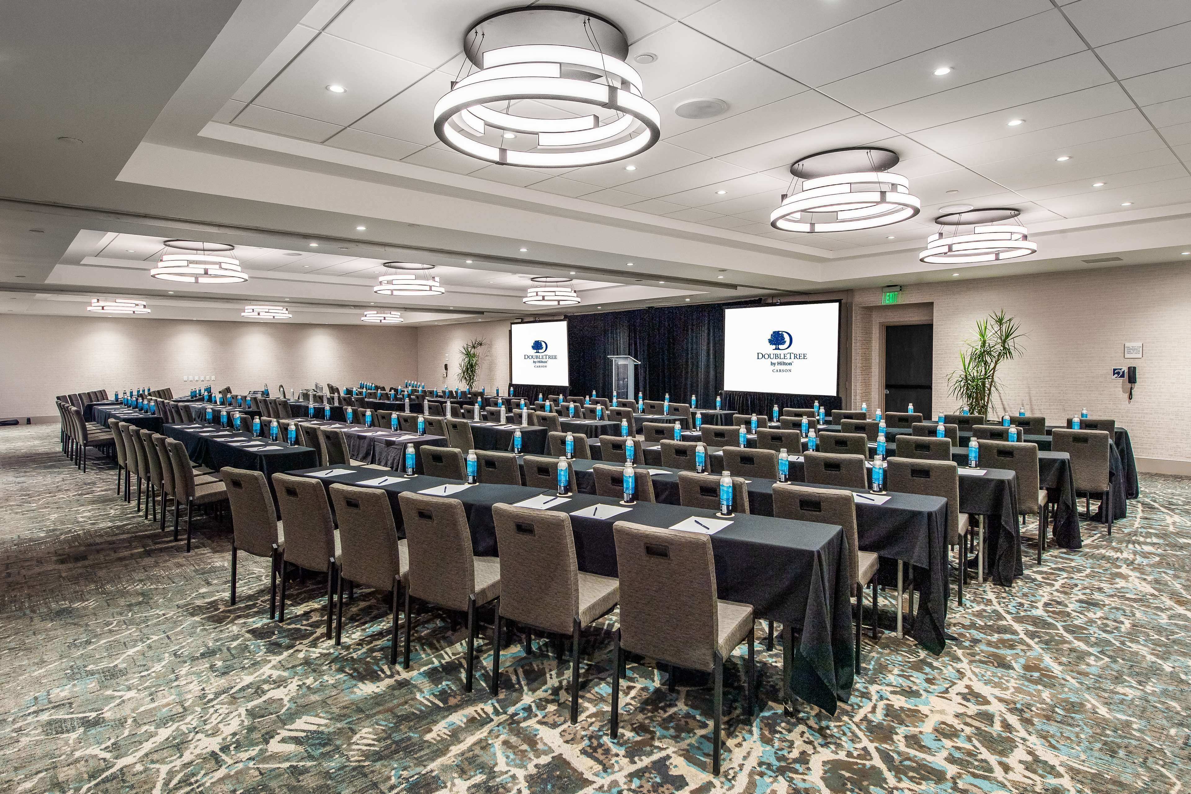 A conference room with rows of tables and chairs, equipped with water bottles, and a large screen displaying the Doubletree logo.