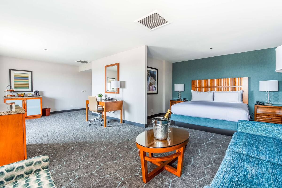 Habitación de hotel con cama, escritorio, silla, mesita con una botella y sofá.