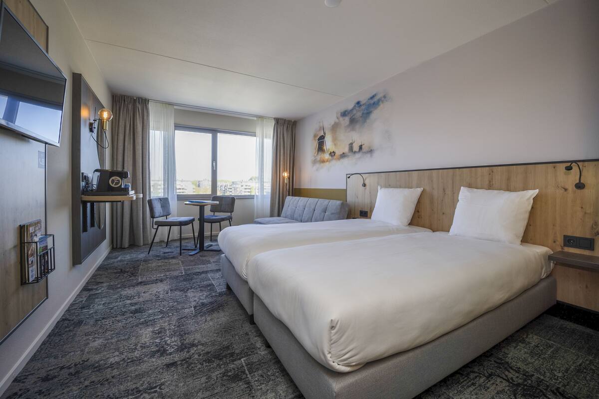 Une chambre d’hôtel avec deux lits, un bureau, une chaise, une télévision et une vue sur la ville.