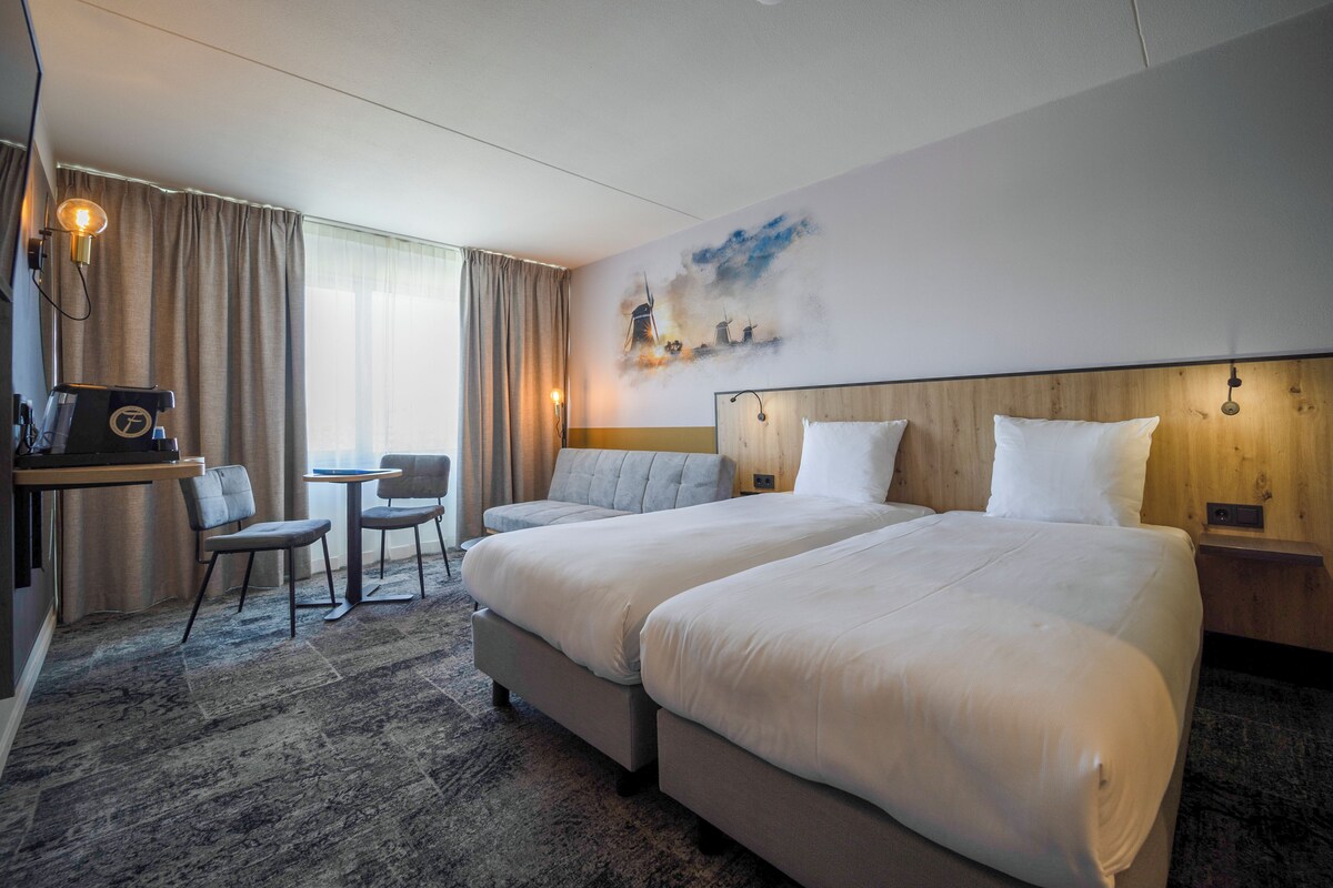 Een hotelkamer met twee bedden, een bureau, een stoel en een klein tafeltje.