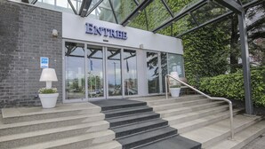 Een gevel met de naam 'ENTREE' boven de deuren, een trap die erheen leidt, en een bloempot links.